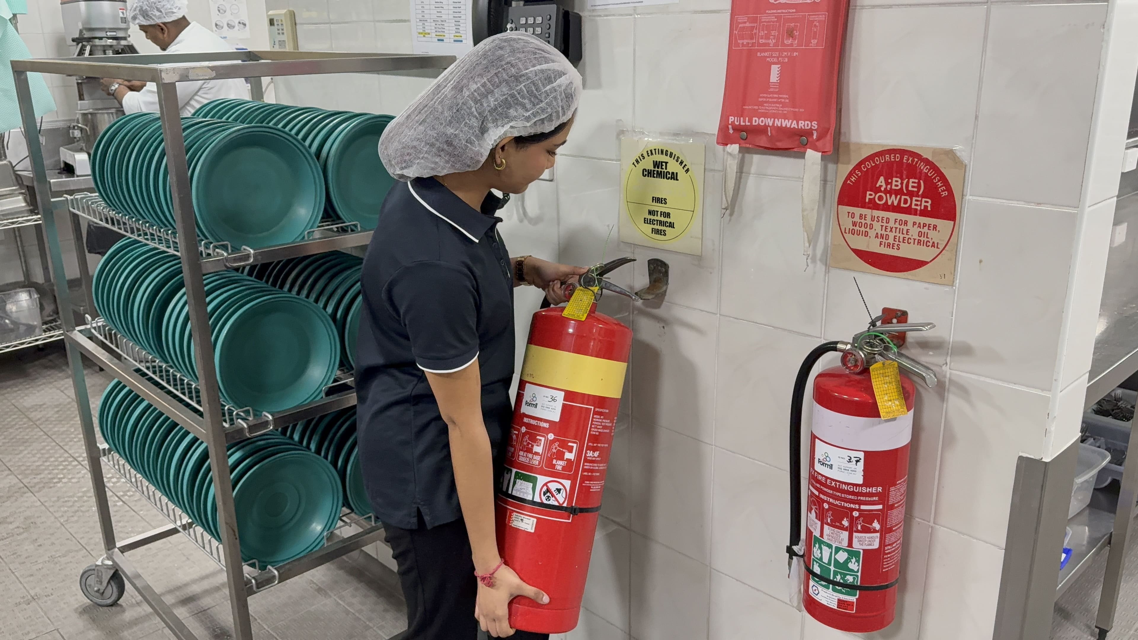 Aged care staff member taking down a fire extinguisher in a kitchen
