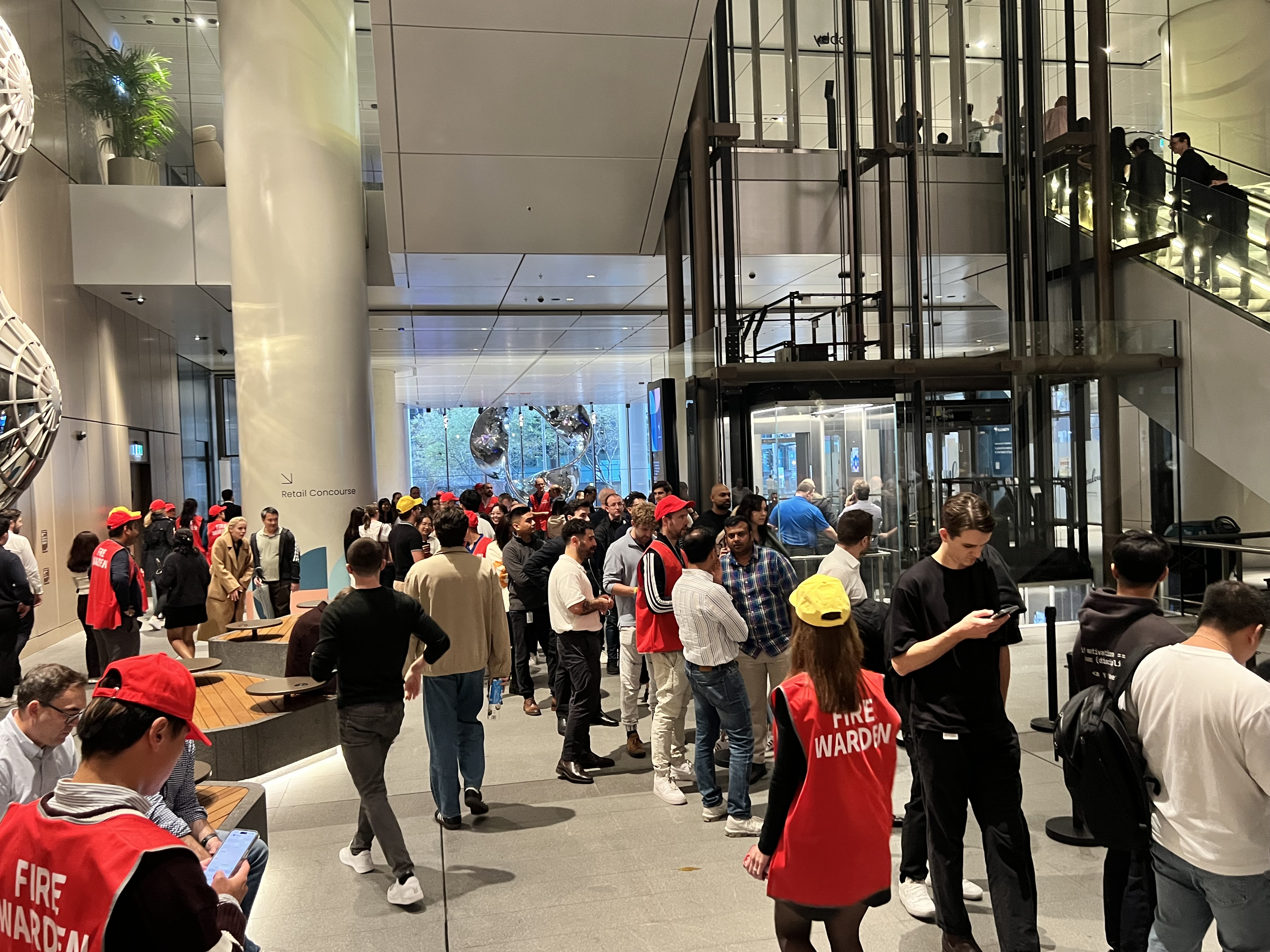 Wardens in red and yellow vests gathering evacuated staff in a building foyer