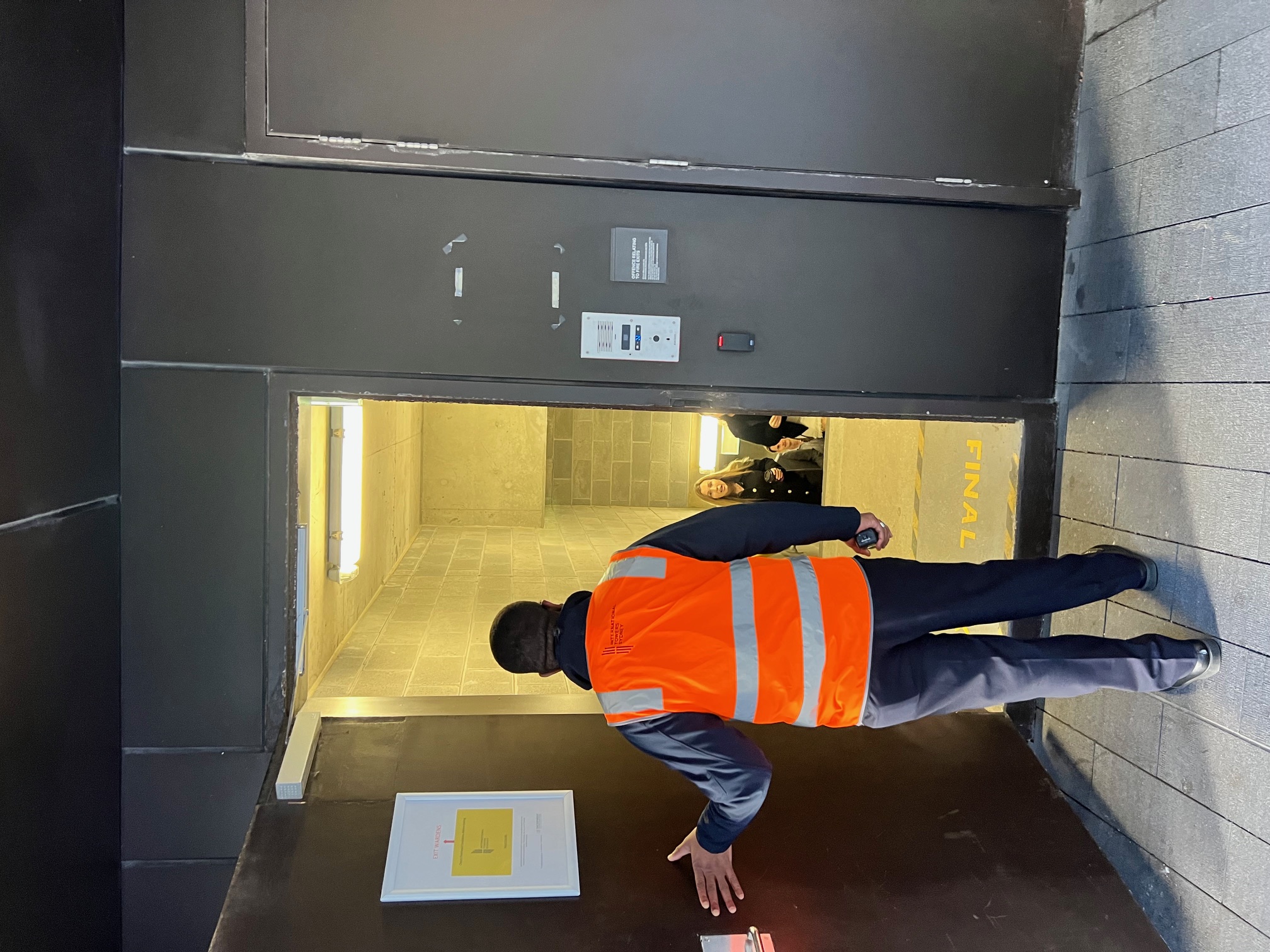Warden in an orange vest checking a building exit door